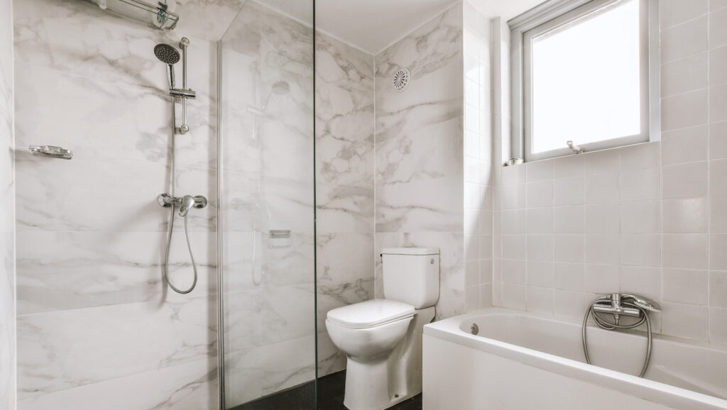 Flush toilet located between sink and shower in small tiled bathroom of contemporary apartment